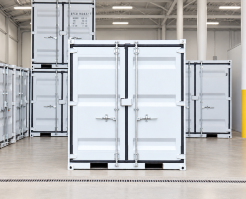 Seasonal Storage 7 x 8 Container A white shipping container stands in a clean, bright warehouse with other stacked containers visible in the background. The floor is polished concrete and a yellow column is to the right.